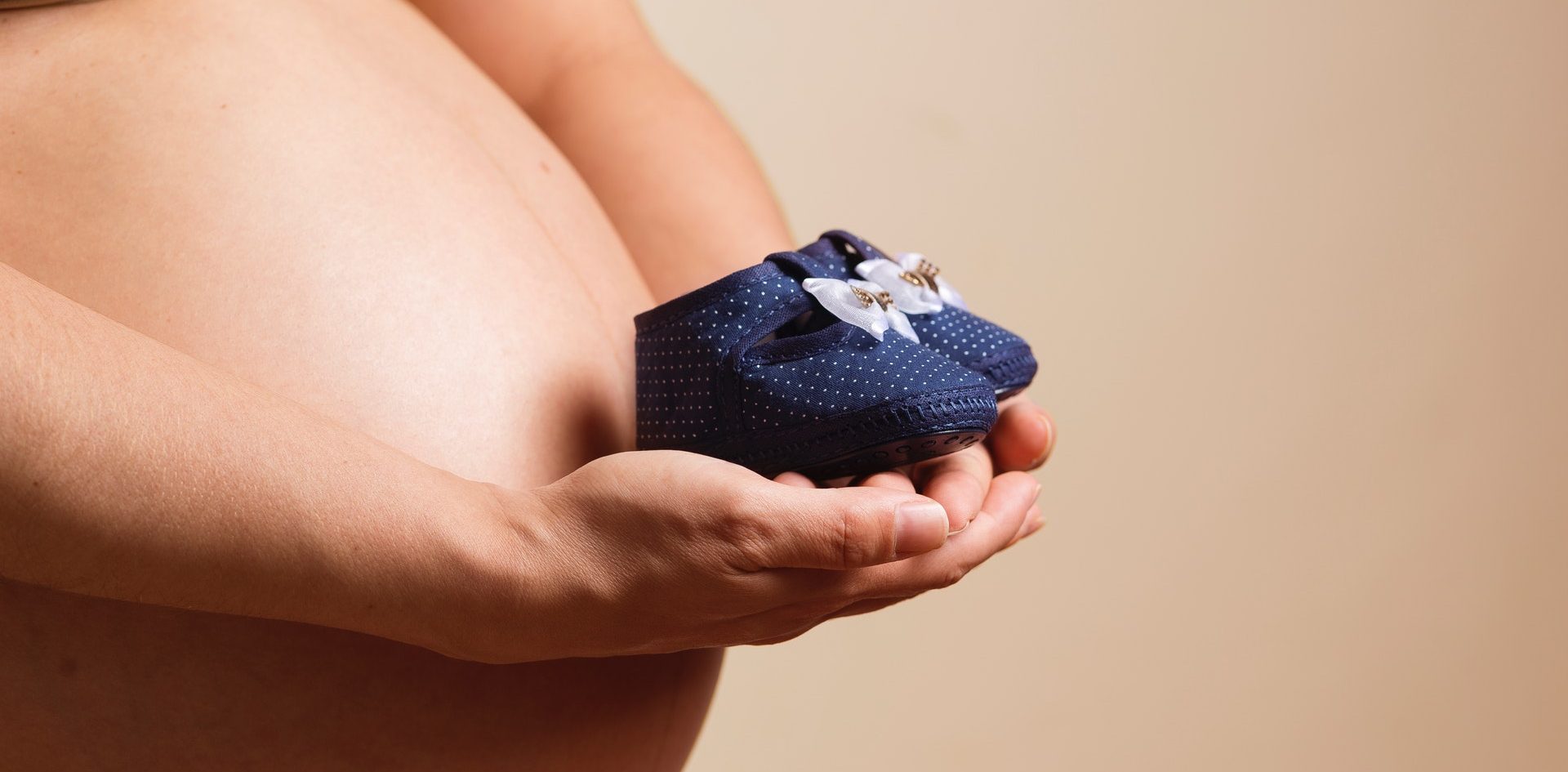 Schwangere Frau hält baby schuhe in der Hand
